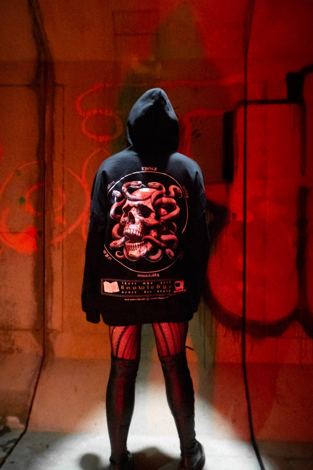 Female model back view wearing the Dark Matter Threads Knowledge unisex hoodie in black ,featuring back graphic artwork.