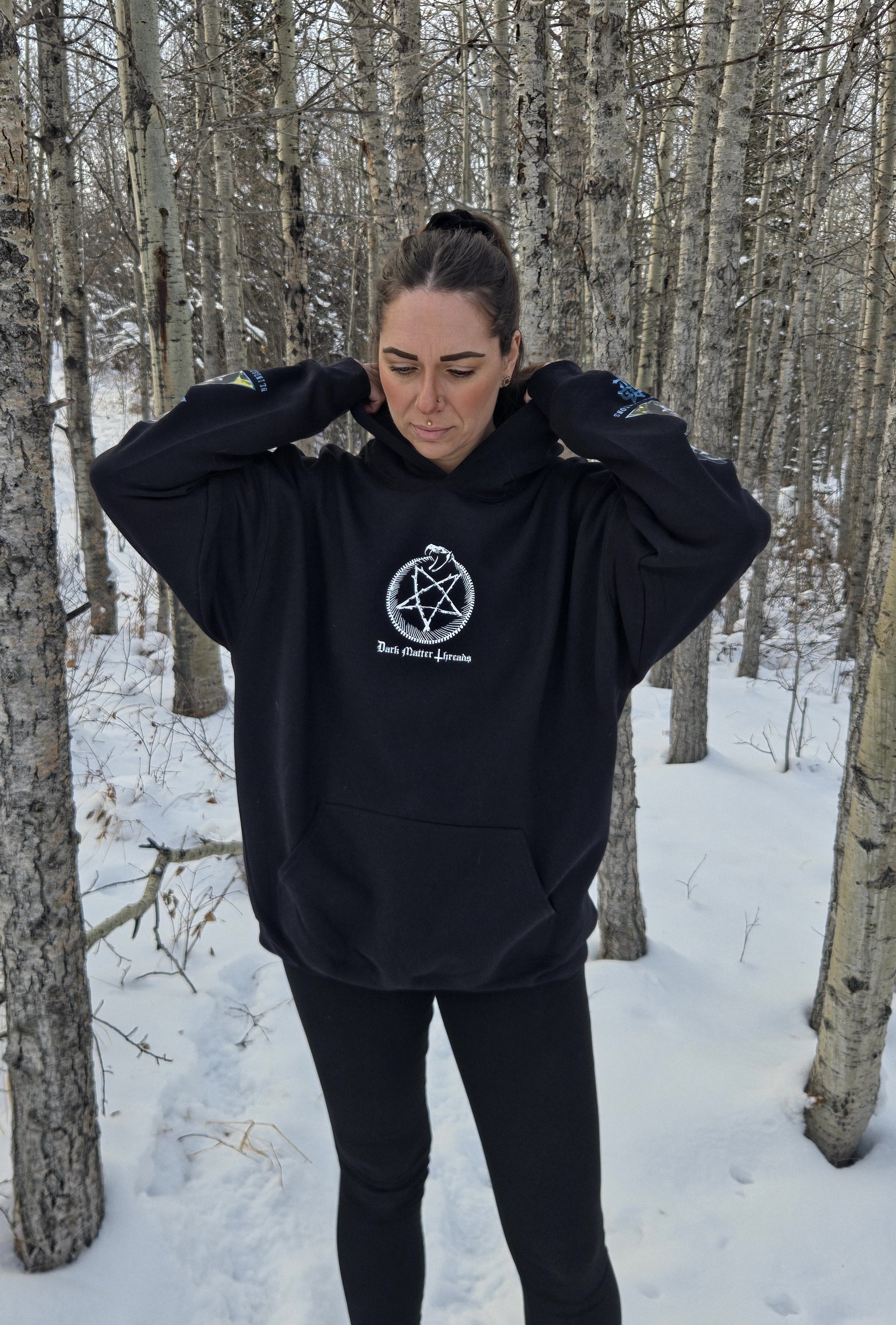 Female model wearing the Dark Matter Threads black unisex graphic hoodie, front view with front and sleeve designs, streetwear fit.