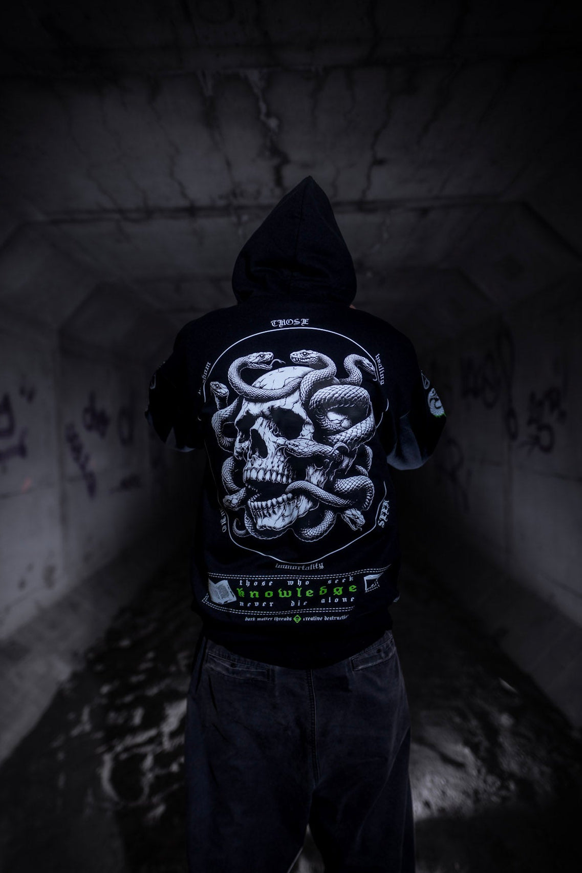 Male model back view wearing the Dark Matter Threads Knowledge black unisex hoodie with the hood up and back graphic design.