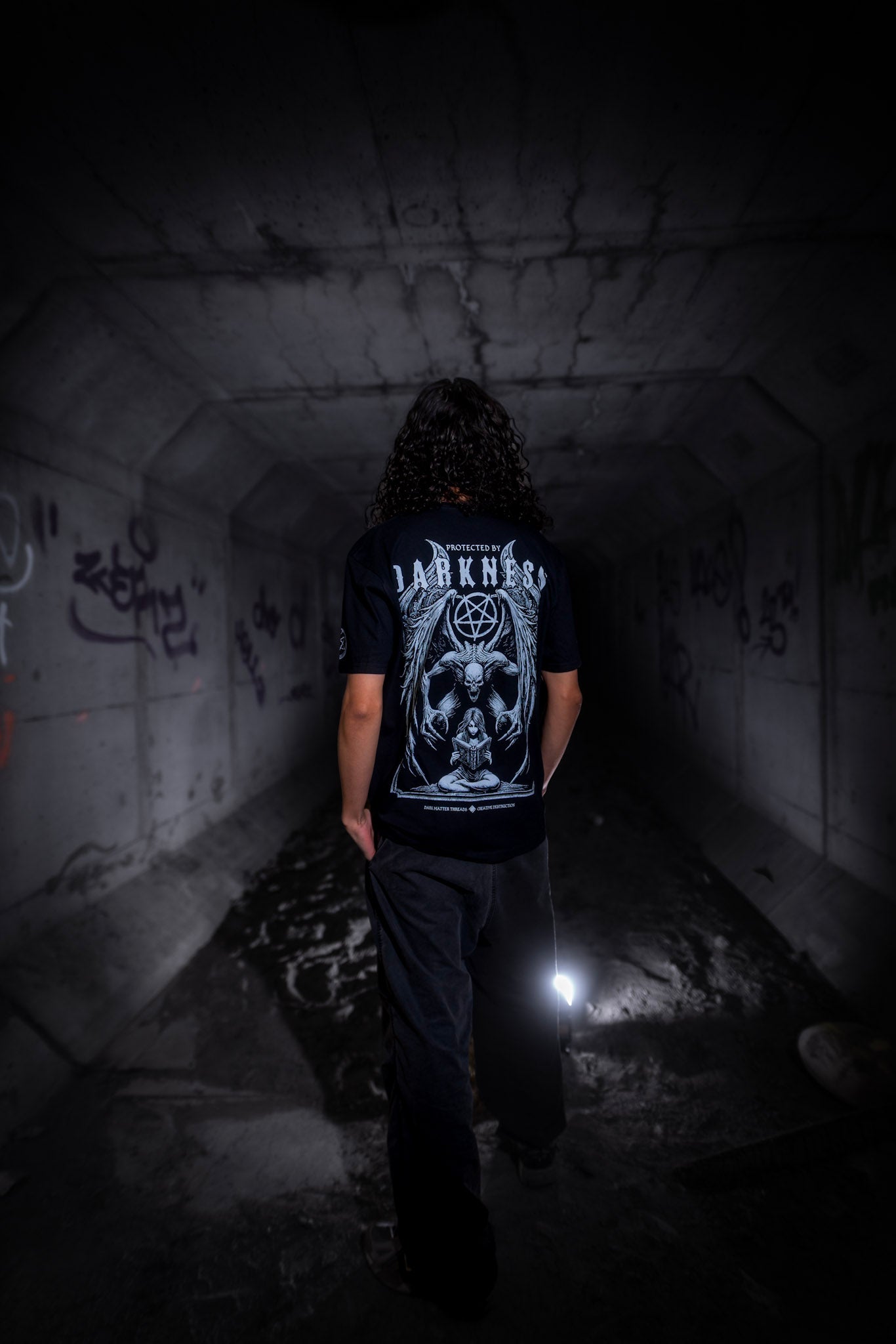 Male model back view wearing the Dark Matter Threads Protected graphic printed unisex t-shirt, 100% cotton.