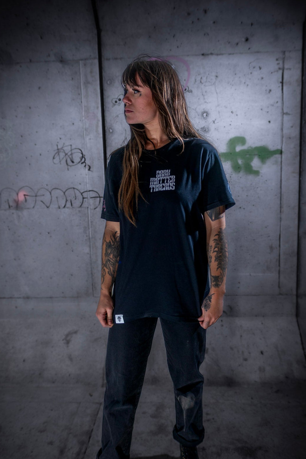 Female model front view wearing the Dark Matter Threads Trapped in Reality unisex t-shirt in black, featuring the back graphic, 100% cotton.
